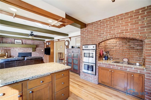 kitchen featuring light wood-type flooring, beam ceiling, double oven, brick wall, and ceiling fan