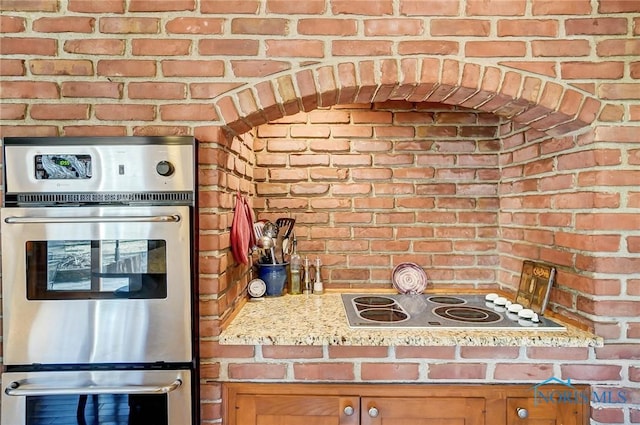 kitchen featuring double oven, electric stovetop, brown cabinetry, and brick wall