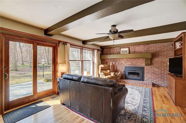 living room with ceiling fan, beamed ceiling, light wood-style flooring, and a fireplace