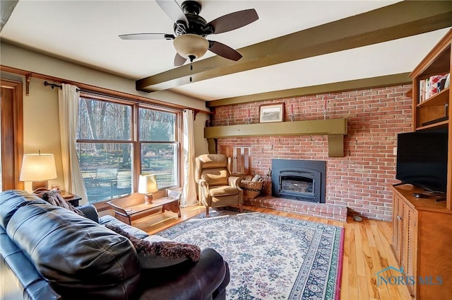 living room featuring beam ceiling, a brick fireplace, wood finished floors, and ceiling fan