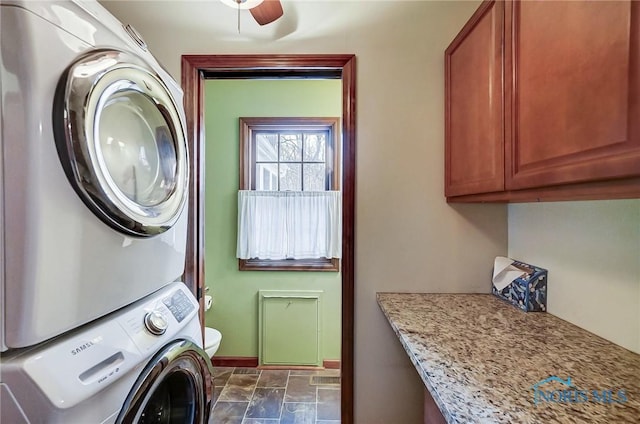 laundry area with cabinet space, baseboards, stacked washer / drying machine, and stone finish floor