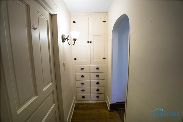 hallway featuring baseboards, arched walkways, and dark wood-style floors