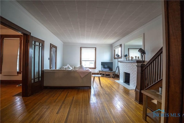 living area featuring baseboards, ornamental molding, stairs, dark wood-type flooring, and a brick fireplace