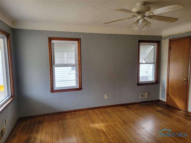 unfurnished room with visible vents, baseboards, wood finished floors, and a ceiling fan