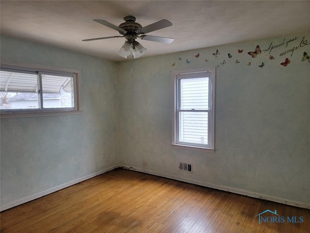 unfurnished room featuring a wealth of natural light, visible vents, hardwood / wood-style floors, and ceiling fan