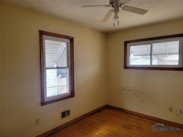 unfurnished room featuring ceiling fan, visible vents, baseboards, and wood finished floors