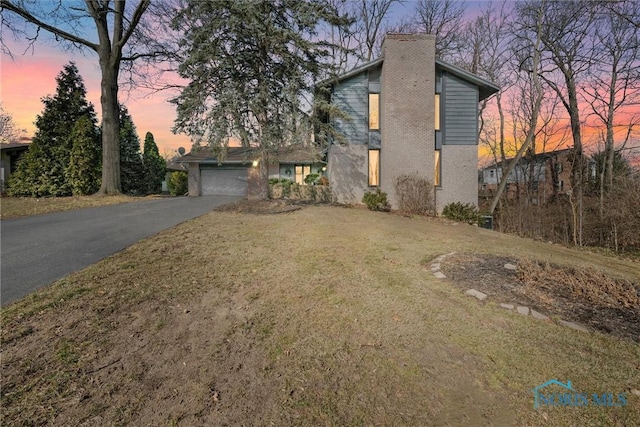 traditional-style house with aphalt driveway, a chimney, a front yard, and a garage