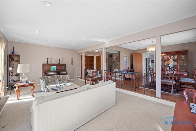 carpeted living area with an inviting chandelier and stairway