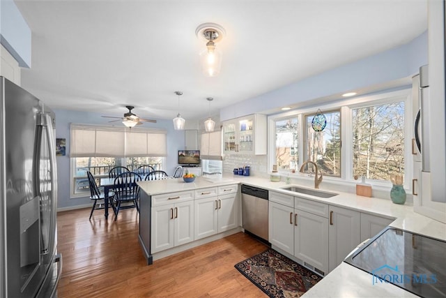 kitchen with a peninsula, light wood finished floors, appliances with stainless steel finishes, and a sink