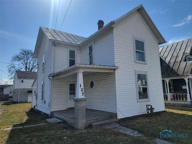 view of home's exterior featuring a standing seam roof, a porch, a yard, metal roof, and a chimney