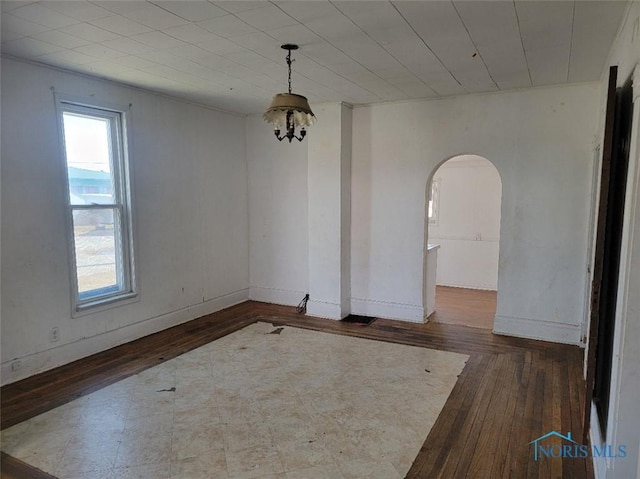 spare room with a notable chandelier, wood finished floors, arched walkways, and baseboards