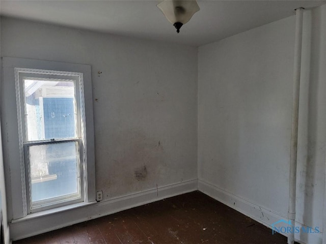 spare room featuring dark wood finished floors, a healthy amount of sunlight, and baseboards