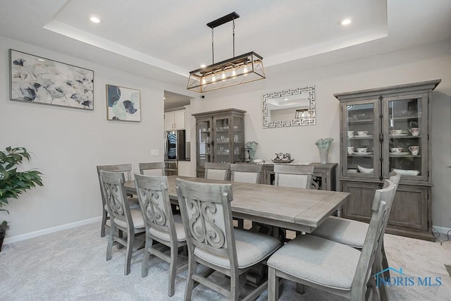 dining space with baseboards, light colored carpet, a tray ceiling, recessed lighting, and an inviting chandelier