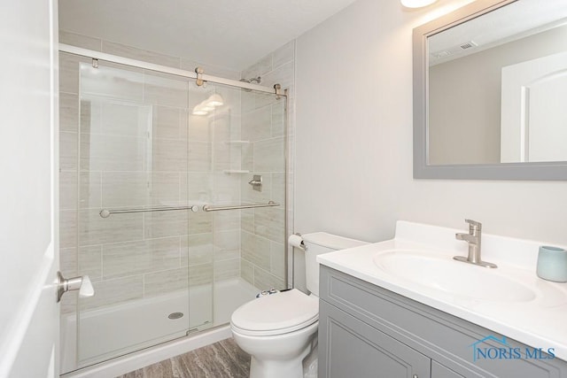 bathroom with visible vents, toilet, a stall shower, wood finished floors, and vanity