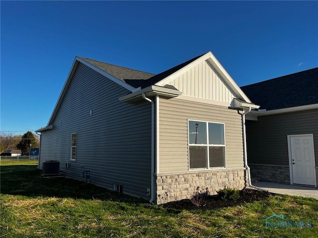 view of side of home featuring stone siding, a lawn, central air condition unit, and board and batten siding