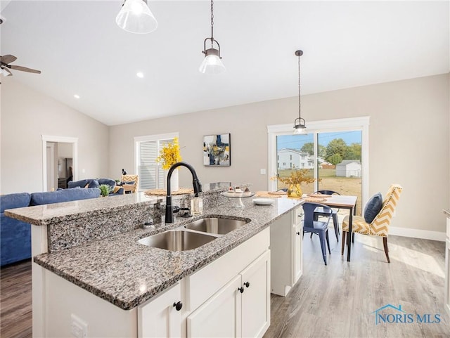 kitchen featuring open floor plan, an island with sink, vaulted ceiling, light wood-style floors, and a sink