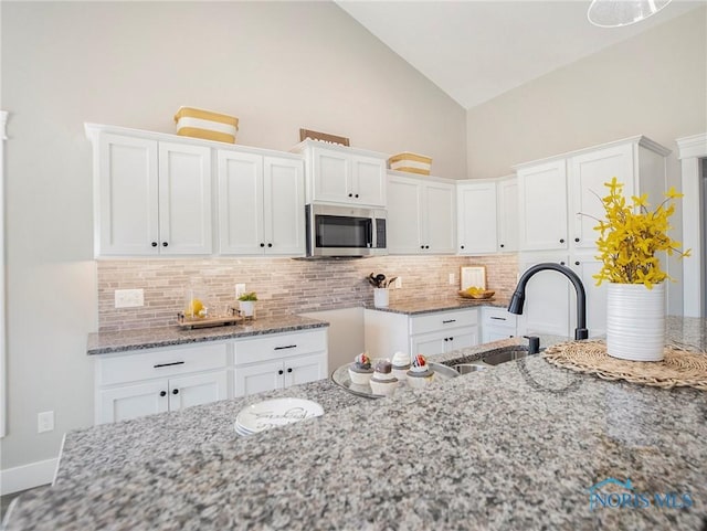 kitchen featuring light stone counters, stainless steel microwave, white cabinetry, and a sink