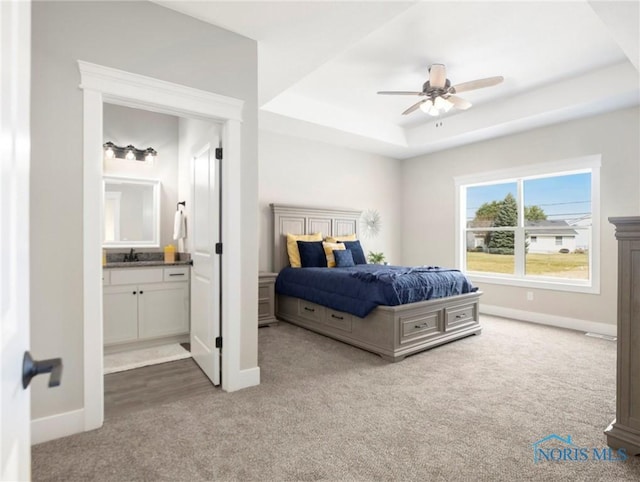 carpeted bedroom with a tray ceiling, baseboards, and ensuite bathroom