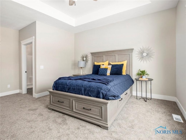 carpeted bedroom with a ceiling fan, a tray ceiling, visible vents, and baseboards