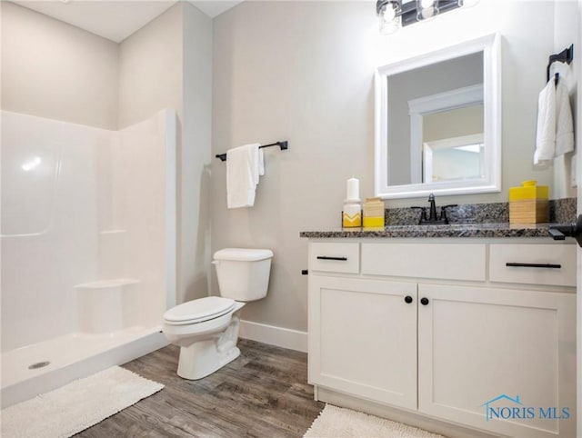 bathroom with toilet, a stall shower, wood finished floors, baseboards, and vanity