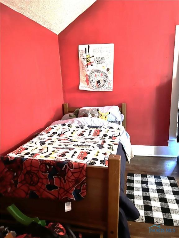 bedroom with wood finished floors, baseboards, and vaulted ceiling