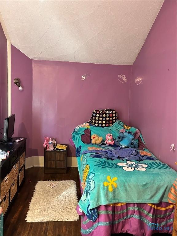 bedroom with vaulted ceiling, wood finished floors, baseboards, and a textured ceiling