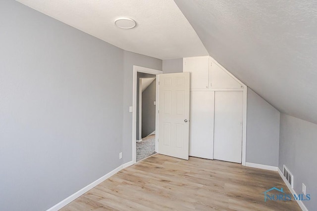 bonus room with visible vents, lofted ceiling, a textured ceiling, light wood finished floors, and baseboards