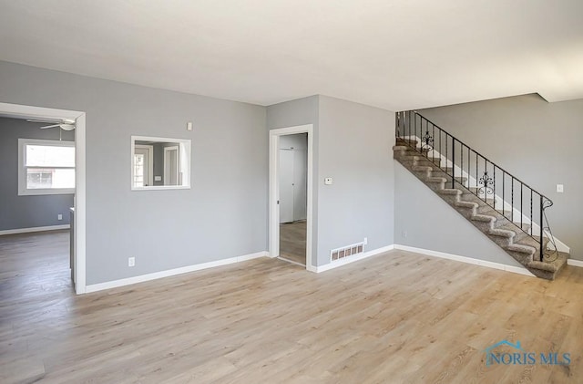 unfurnished living room with light wood-type flooring, visible vents, baseboards, and stairway