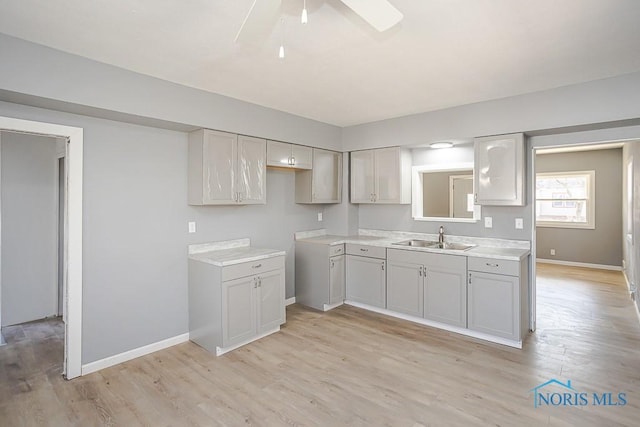 kitchen with a sink, light wood-type flooring, baseboards, and ceiling fan