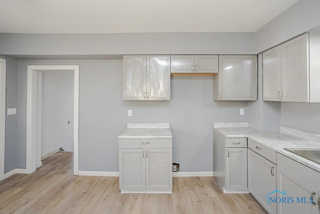 kitchen with a sink, baseboards, light countertops, and light wood finished floors