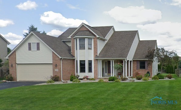 view of front of property with brick siding, a front lawn, an attached garage, and driveway