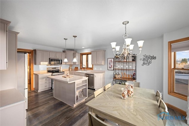 kitchen with appliances with stainless steel finishes, a center island, dark wood finished floors, a sink, and light countertops