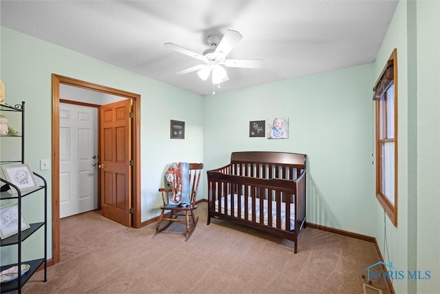 bedroom with a ceiling fan, baseboards, a crib, and carpet