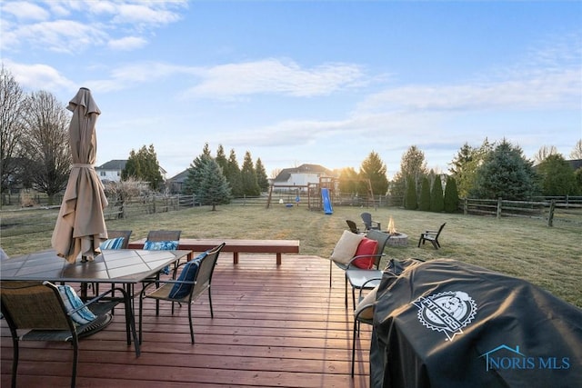 wooden terrace with a lawn, a fenced backyard, a playground, and a fire pit