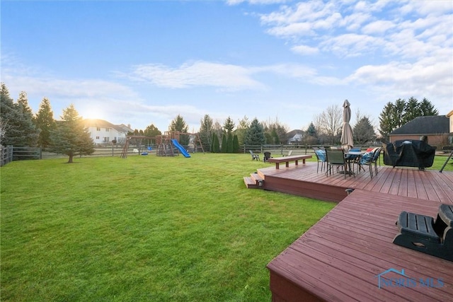 view of yard featuring a deck, outdoor dining area, a fenced backyard, and a playground