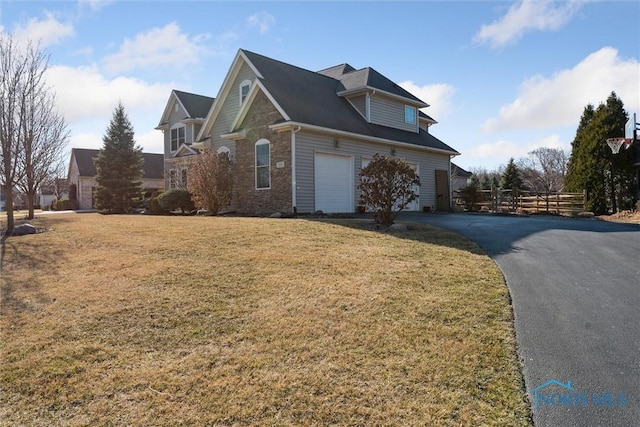 view of side of property with fence, aphalt driveway, a lawn, stone siding, and an attached garage