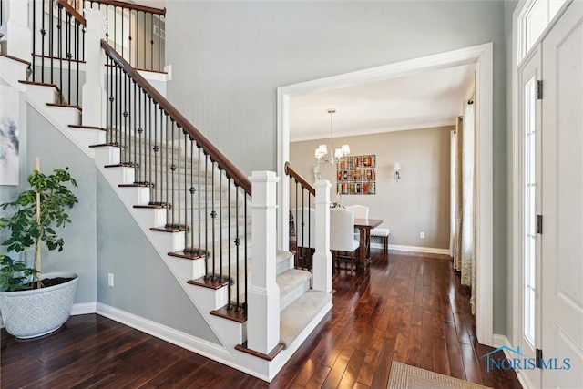 foyer entrance with ornamental molding, hardwood / wood-style floors, an inviting chandelier, baseboards, and stairs