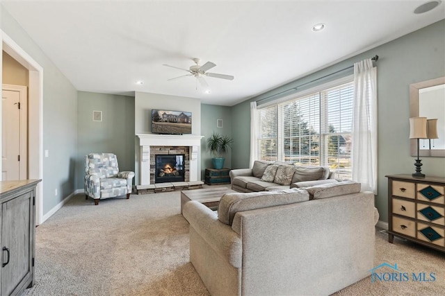 living room featuring baseboards, ceiling fan, light colored carpet, a stone fireplace, and recessed lighting