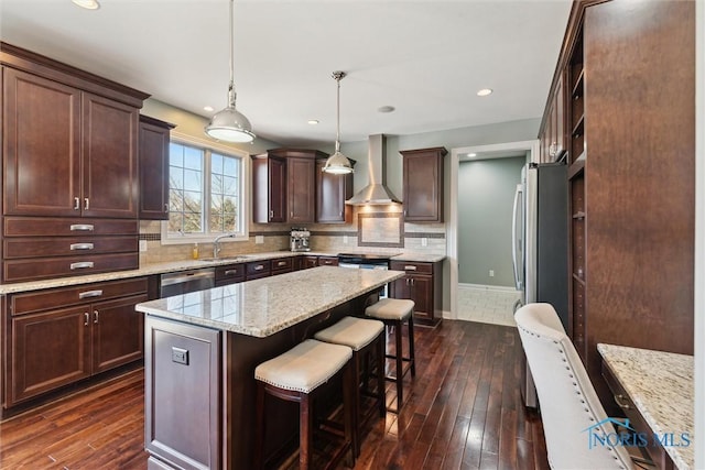 kitchen featuring a breakfast bar, a sink, stainless steel appliances, wall chimney exhaust hood, and backsplash