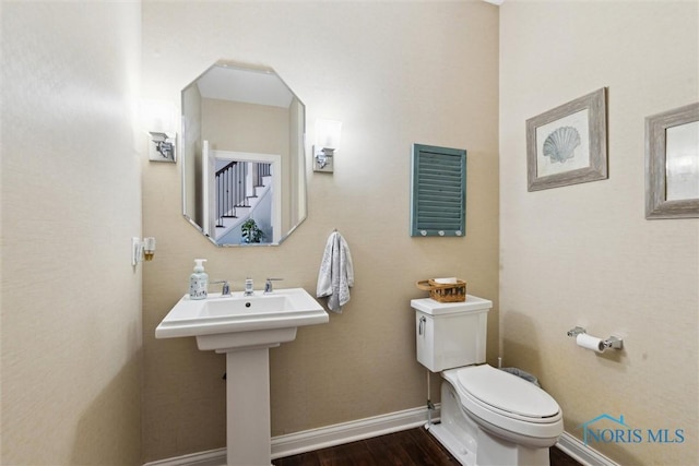 half bathroom with baseboards, toilet, and wood finished floors