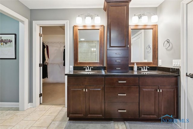 bathroom featuring double vanity, a spacious closet, baseboards, and a sink