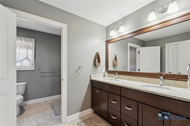 bathroom with a sink, baseboards, toilet, and double vanity