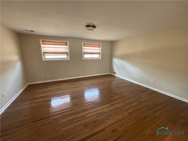 spare room with visible vents, baseboards, and dark wood-style flooring