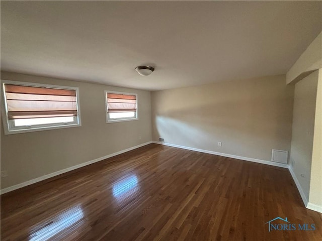 empty room with visible vents, dark wood-style floors, and baseboards