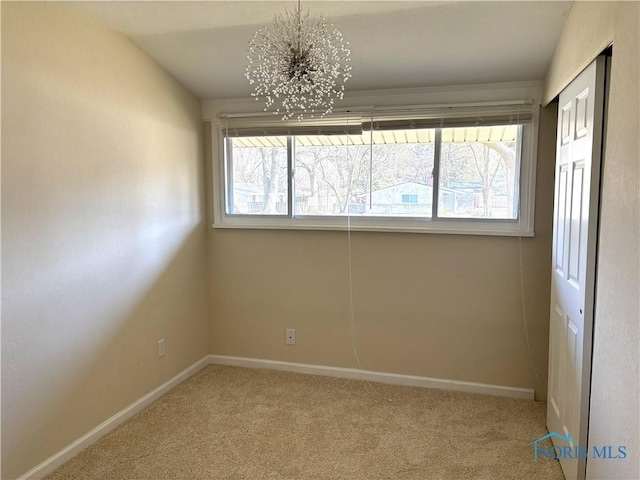 carpeted spare room featuring baseboards, a healthy amount of sunlight, and an inviting chandelier