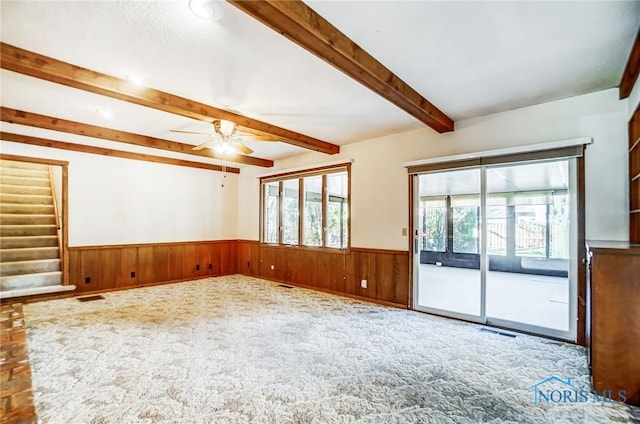 empty room featuring visible vents, beam ceiling, a ceiling fan, wainscoting, and stairs