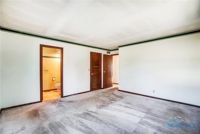 interior space featuring a closet, connected bathroom, light colored carpet, and baseboards