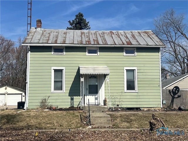 view of front of property with a standing seam roof, a chimney, an outdoor structure, and fence