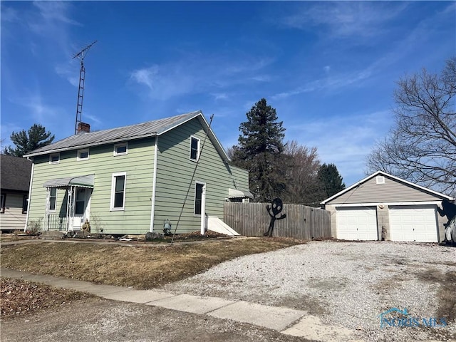 view of home's exterior featuring an outbuilding, fence, a chimney, a detached garage, and metal roof