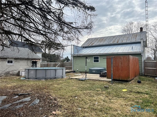 rear view of house with an outbuilding, fence, a fenced in pool, a lawn, and metal roof